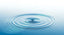 Concentric ripples spreading across a calm blue water surface, evoking sound waves traveling through water