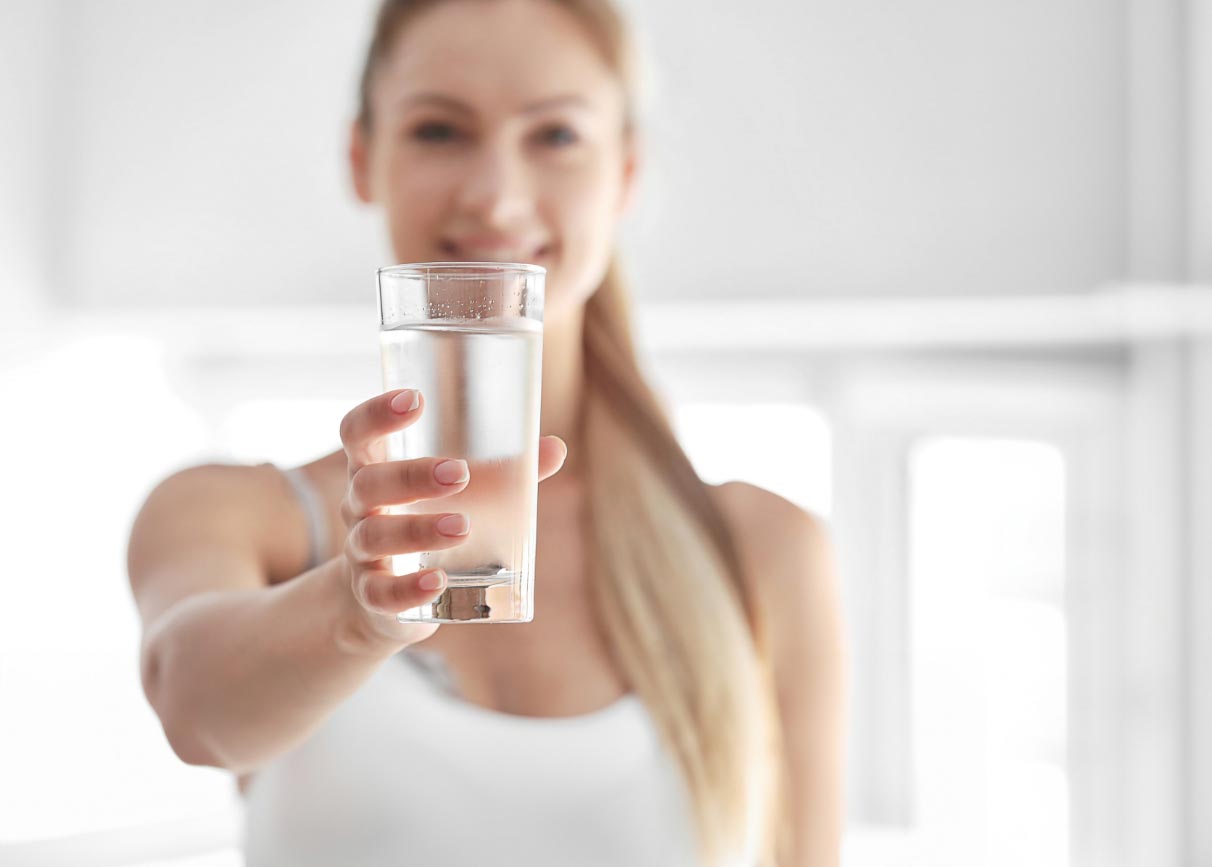 A girl holding a glass of water as if an invitation for you to drink it.